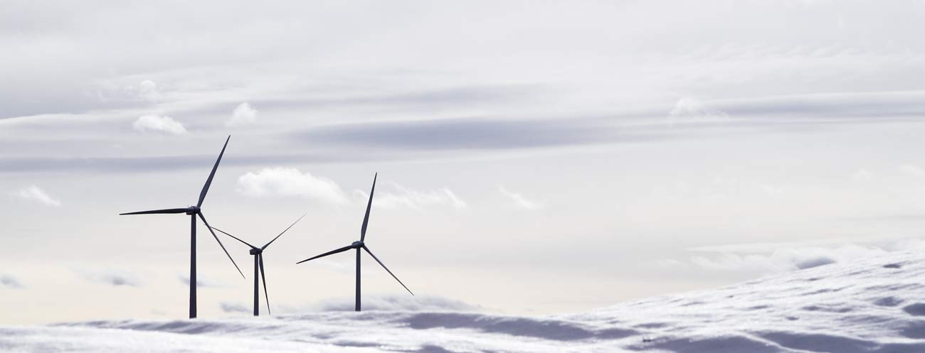 Photography of aerogenerator electric windmills behind lurred snow mountains or clouds. Suggesting open space and strategy.