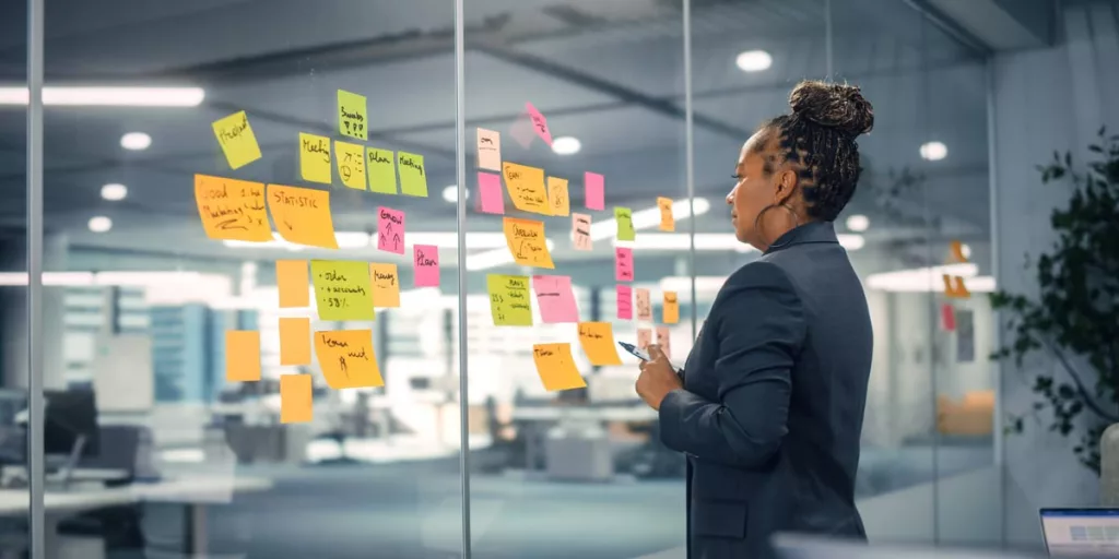Business woman in an office, working using post-notes on a glass wall.