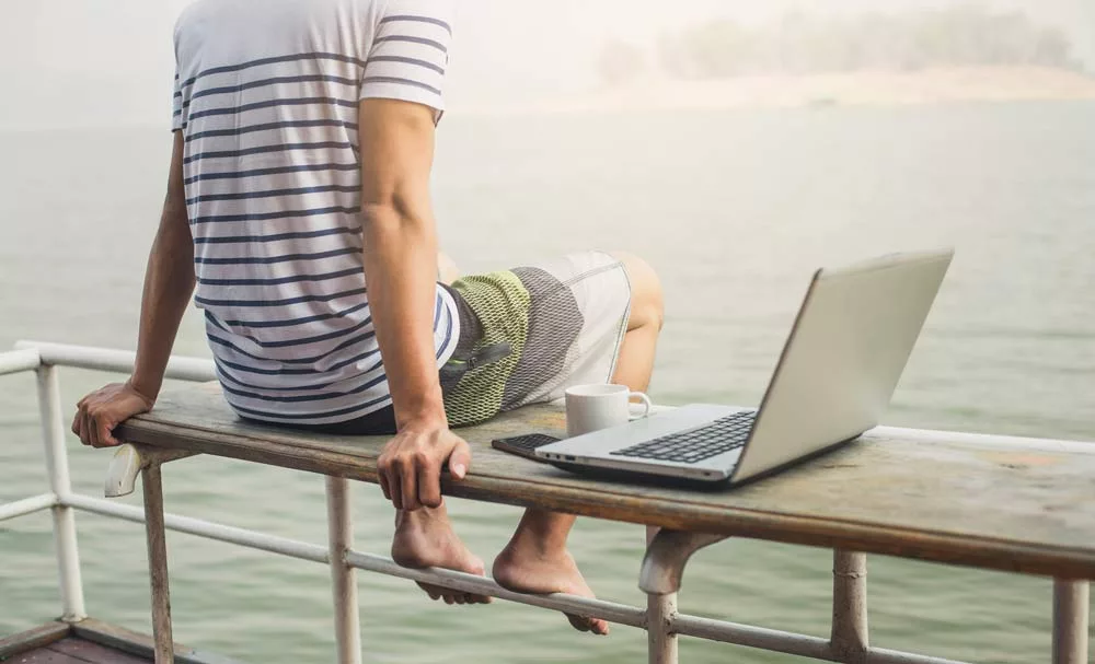 Man sitting at the water, laptop and coffee next to him